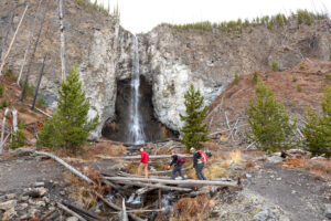 Hikers cross a log bridge below a waterfall Image: NPS / Jacob W. Frank