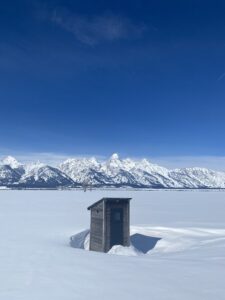 Outhouse in snow with Teton Range behind.