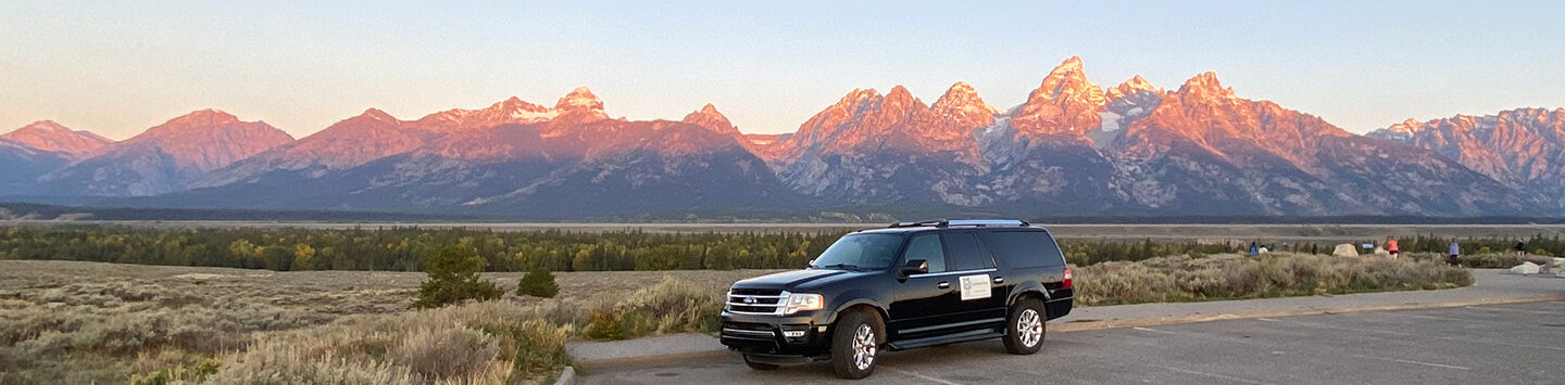 A luxurious Guides of Jackson Hole Ford Expedition in front of the Teton Mountains at Dawn